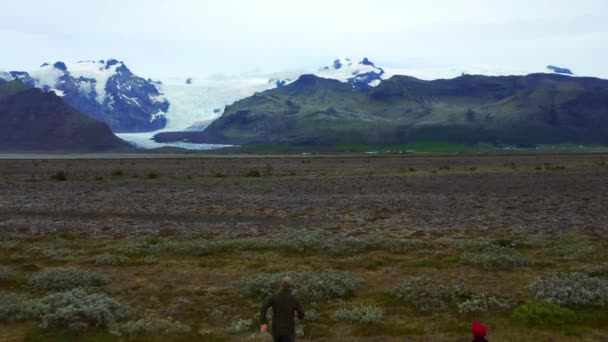 遠くにSvinafellsjokull氷河とSkidarsandurでフィールド上で実行している男性 — ストック動画