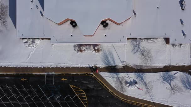 最近の降雪の後の明るい日に ニューヨーク州ベイショアの学校の上空の無人偵察機の眺め 雪ブロワーで歩道をクリアしている保護者の上にまっすぐ下に傾いた場所にカメラのホバー — ストック動画