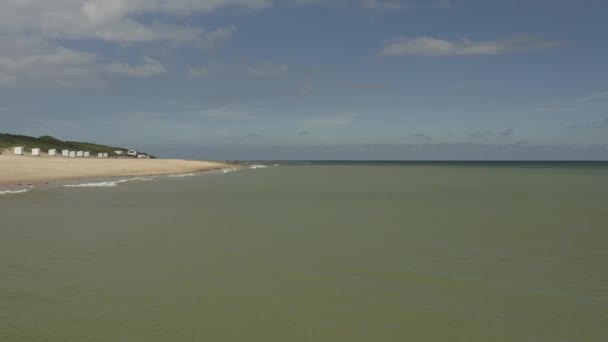 晴れた日に美しいビーチを歩く女性に向かって波の上を横に移動する空中ショット — ストック動画