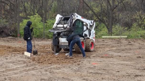 Two Construction Workers Watch Skid Steer Loader Hydraulic Auger Approaches — Stock Video