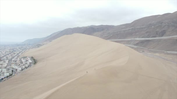 タラパカ チリのイキケの現代都市で有名なセララ ドラゴンの空中ドローンショット 市内の曇りの午後をよりよく見るために砂丘の頂上をハイキングする観光客 — ストック動画