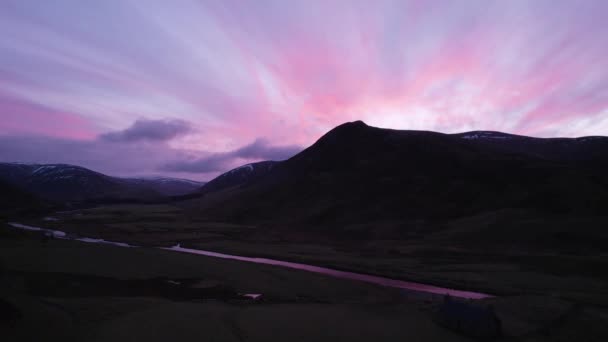 日没が川と雲の中を反射するので シルエットになった山々に向かって見て強烈なピンクと紫の日没の間にスコットランドのグレンシーでゆっくりと上昇する空中ドローン映像 — ストック動画