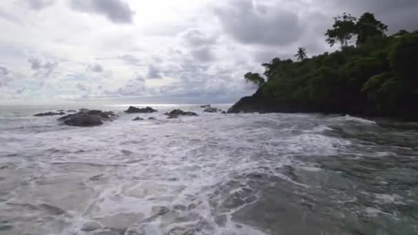 コスタリカのドミニカリトビーチで曇りの日に岩の多い海岸線を打つ海の波の上を飛行中の空中ドリー — ストック動画