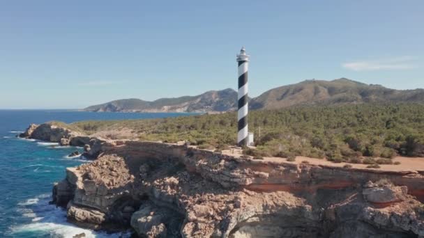 スペインのイビサ島のプンタ モスカーター灯台に傾斜空中ビュー 澄んだ海と空を示す灯台の周りに 荒波が崖にぶつかっている 鳥が飛び立つ — ストック動画