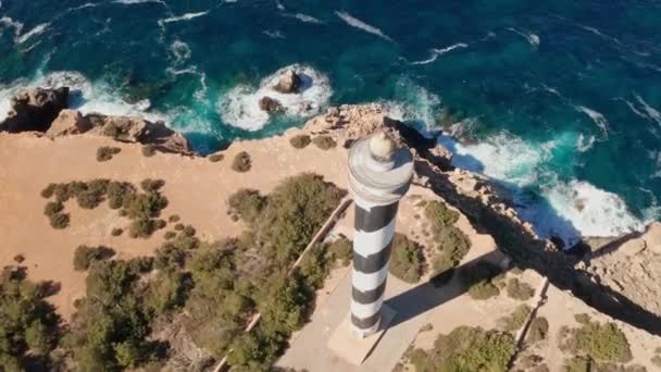 スペインのイビサ島にあるプンタ モスカーター灯台に傾斜している空中ビュー 灯台は近くにあり 澄んだ海と空 崖に打ち寄せる荒波を見せています — ストック動画