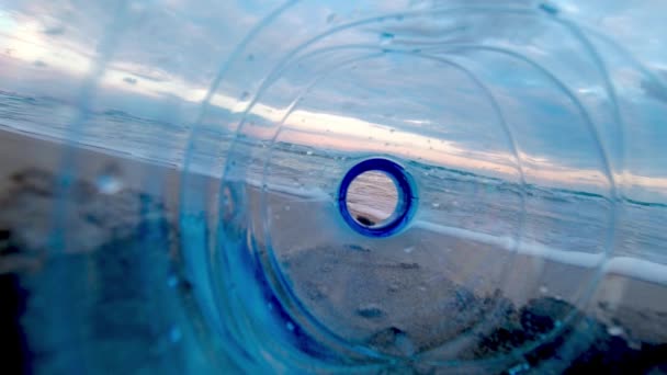 海の環境を台無しにする廃プラスチックボトルを通して見られるようにビーチでの日没 スローモーション — ストック動画