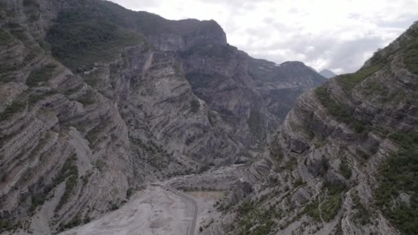 曇りの空と曲がりくねった道の高さでアルバニアの山とセミ川の間のSh20道路上の発見を進める前面飛行機のドローンビデオ — ストック動画