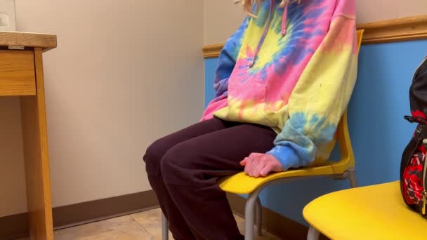 医生医院的办公室里 戴着眼镜片的小男孩或小女孩紧张地坐在黄色椅子上 手忙脚乱地挥动拳头 坐在座位上 — 图库视频影像
