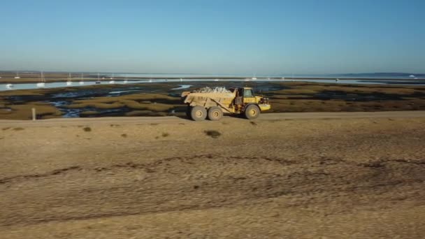 海の近くのビーチを運転する大型ダンパートラックの映像のドローン追跡ショット — ストック動画