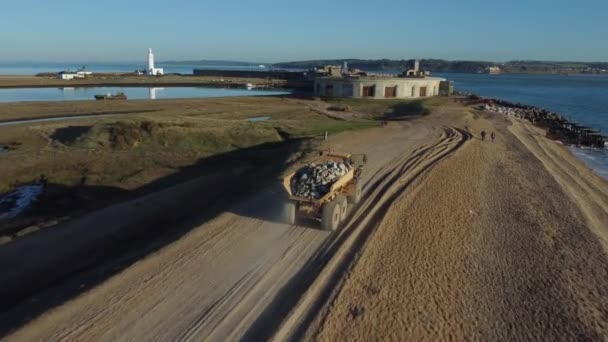 海沿いのビーチを城に向かって走る岩だらけの大型ダンパートラックの映像のドローン追跡 — ストック動画