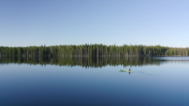 在阳光明媚的一天 身穿绿色皮划艇的人平静地划过一个非常平坦的湖 在芬兰美丽的自然中反映出森林的边缘 无人机玩具枪 — 图库视频影像
