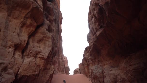 バックビューロンリーマンの深い砂岩の崖の下のキャニオンで砂の上を歩く Wadi Rum Jordan スローモーションワイドビュー — ストック動画