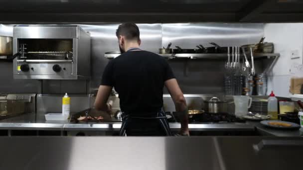 在商业厨房工作的年轻男性厨师翻动熏肉 — 图库视频影像