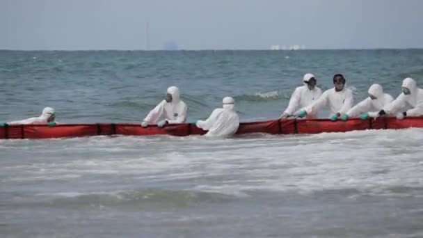 Ppeスーツの海軍将校は タイのラヨーンで水中パイプラインの漏れのためにビーチへのオイルブームを一緒に働いて引っ張っ ワイドショット — ストック動画