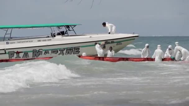 ラヨーンの海岸で石油ブームの障壁を解消するのに役立つスピードボートに燃料のガロンをロードするPpeスーツの海軍 — ストック動画