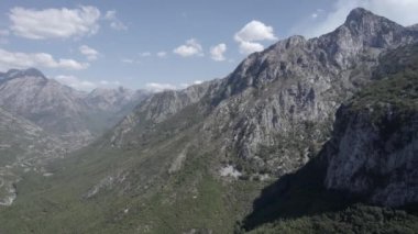 Lumi I thethit nehrinin üzerinde hareket eden önden drone videosu var. Ana çekim olarak dağların önündeler. Plan dağa çok yakın bitiyor..