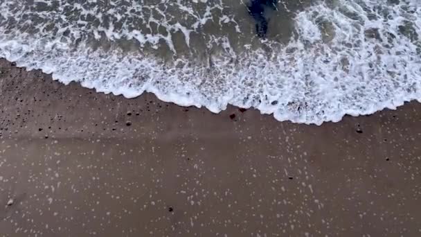 茶色の砂のビーチの端に泡が打ち寄せる波が海の亀裂を引き — ストック動画