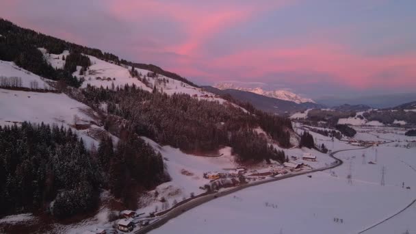 雪に覆われた山間の町の空中ショットは 日没時に谷を通って道路を巻き — ストック動画