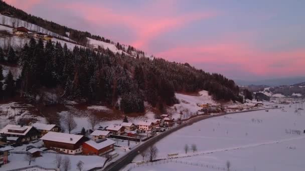 雪に覆われた山間の町の空中ショットは 日没時に谷を通って道路を巻き — ストック動画