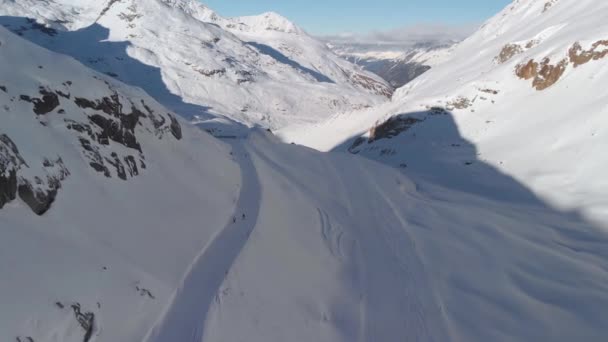 素晴らしい日当たりの良い高山の風景の中に下り坂のスキーヤーを見下ろす空中ドローンビュー — ストック動画