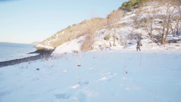 バックパック付きの遠い男雪の山の中で彼の犬ペットとトレック湖畔で ワイドショット — ストック動画
