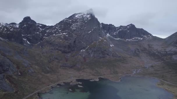 Drohnenaufnahme Einer Straße Unter Steilen Schneebedeckten Bergen Der Wolkenverhangenen Lofoten — Stockvideo