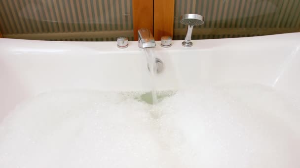Zblízka tekoucí voda ve vaně s pěnou. Příprava koupele doma nebo v hotelu uvnitř.