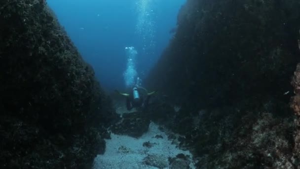 潜水者在深海深处两个高耸的岩层之间游泳的景象 — 图库视频影像