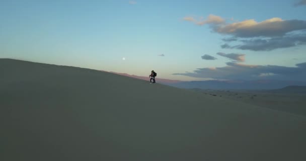 風の強い不毛の砂漠を1人で歩く2人の少年の空中フォローショット デスバレーの背景にカラフルな雲を持つ大砂丘で カリフォルニアUsa — ストック動画