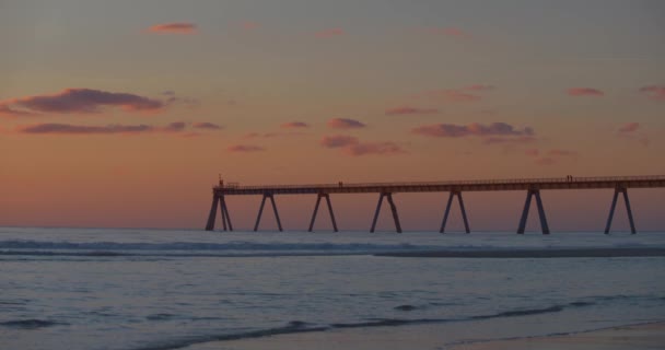 海滩上一片灼热的橙色落日 波浪滚滚 一个长长的码头 — 图库视频影像