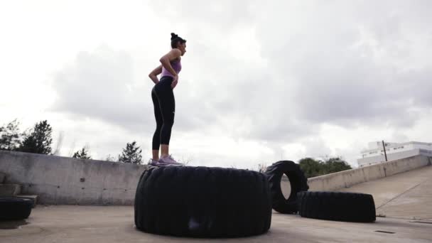 スポーティ女性は タイヤでテラスで筋肉を構築運動 飛び跳ねるスクワット — ストック動画