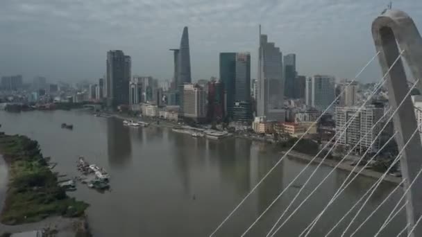 ドローン超高層ビルが青い空と水の上に出荷された川の上に大きな吊り橋を過ぎて市内中心部に向かって飛んでいます 場所ホーチミン市の中心部とベトナムの木Them橋 — ストック動画