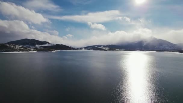 コロラド州ディラン貯水池 曇り空の晴れた日の背景に雪をかぶったロッキー山脈と深い青色の湖を飛んでドローンの空中映像 — ストック動画