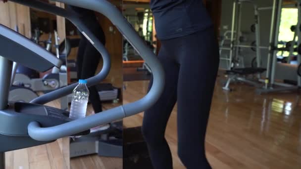 Ноги Тонкой Женщины Упражняются Стационарном Эллиптическом Тренере Водяной Бутылкой Урожай — стоковое видео