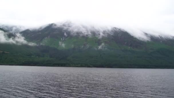 白い雲がゆっくりと高い緑のスコットランドの山々の上を移動し その上は風が水の中に小さな波を吹くと完全に霧に包まれています ワイドショット — ストック動画