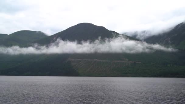 小さな波が水の中で過去に吹き流されるので 低い吊り雲はスコットランド高地の山の中腹でゆっくりと動いています 曇りの日に撮影された — ストック動画