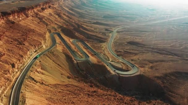 いくつかの車は 美しい茶色の丘の風景の中にイスラエルのミッツェ ラモンの高速道路40にヘアピン曲げと黒のアスファルトに降ります 高角度ドローンショット — ストック動画