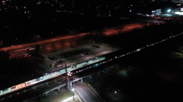 在一个漆黑的冬夜 一个火车站的空中拍摄到一列火车穿过车站 一些停放在停车场里的汽车 无人驾驶相机在火车后面盘旋和平底锅离开了 — 图库视频影像