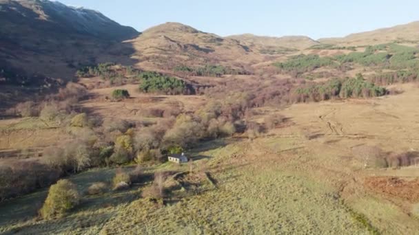 空中无人驾驶飞机镜头下降向当地的林地和一个偏远的苏格兰Bothy 格伦埃里的Cadderlie Bothy 长长的阴影和阳光下的森林山坡 — 图库视频影像