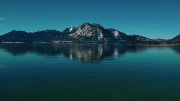 Szcenírozott bajor tó Walchensee Dél-Németországban az Alpokban hegyek közelében Ausztriában. Kék tiszta vízhullámok és idilli kék ég télen. Zökkenőmentes videó hurok cinemthe 4K UHD légi drón.