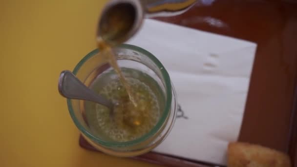 Mátový čaj nalitý z kovové konvice do sklenice na žlutém stole