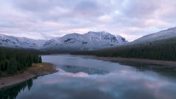 夕暮れ時に雪に覆われた山に向かって湖を飛ぶドローン — ストック動画