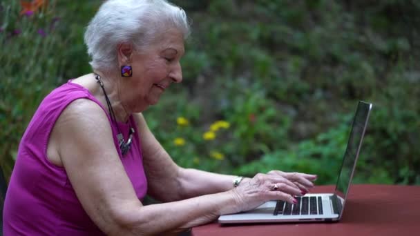 閉鎖側は庭のテーブルでキーボードの外に入力する高齢者の女性を撮影 — ストック動画