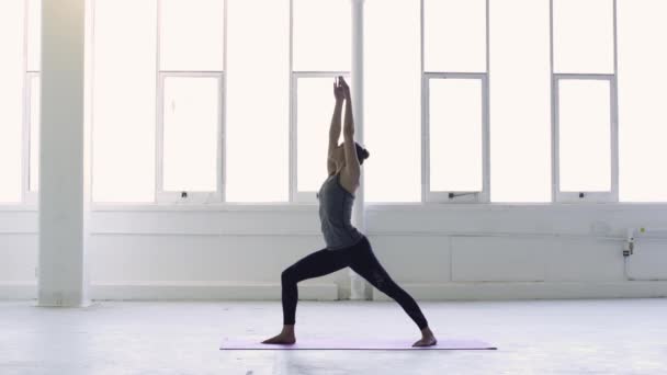 三脚架拍摄的一个年轻的黑发女子练习瑜伽战士序列在一个白色仓库工作室 — 图库视频影像