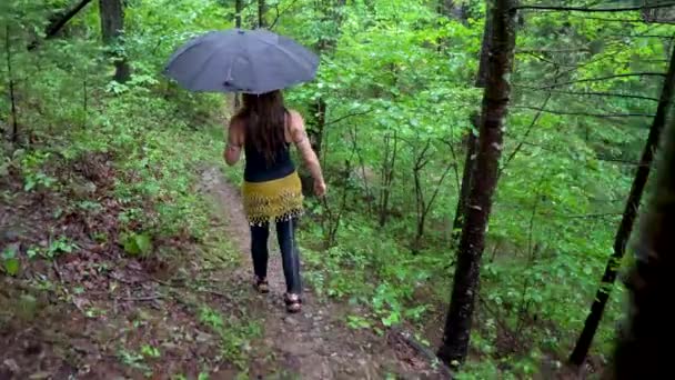 身穿湿衣 手持雨伞 戴着头巾的女人走在远足小径上 — 图库视频影像