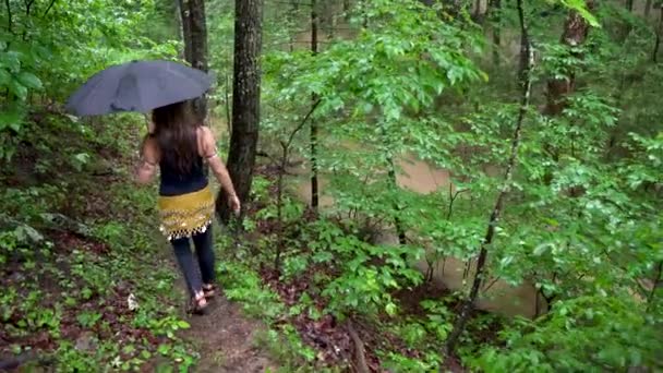ウェットスーツを着て傘を持って腰のスカーフを持つ女性は 側面に水が流れるハイキングコースを歩く — ストック動画