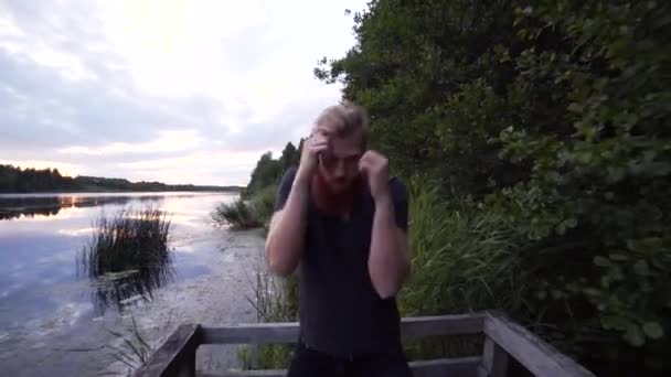 日落时分 在森林里 一个满脸胡须的白人男子在湖边打皮球 面向模型并向后移动的一个稳定的滑行凸轮镜头 — 图库视频影像