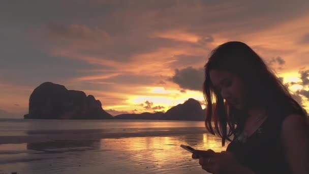 Симпатичная Азиатка Пользуется Мобильным Телефоном Пляже Улыбаясь Красочном Фоне Заката — стоковое видео