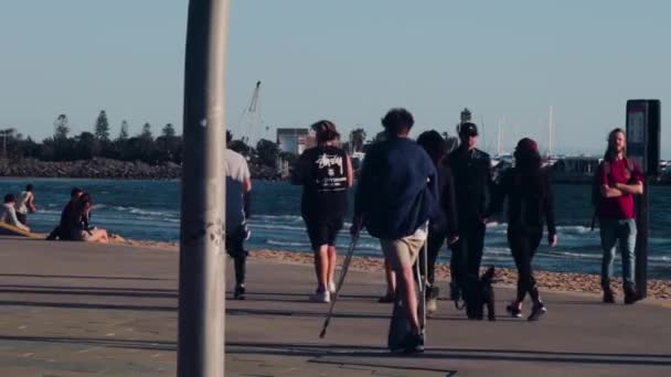在刮风的日子里 留着卷曲头发的年轻人抱着拐杖沿着圣基尔达海滩走着 — 图库视频影像