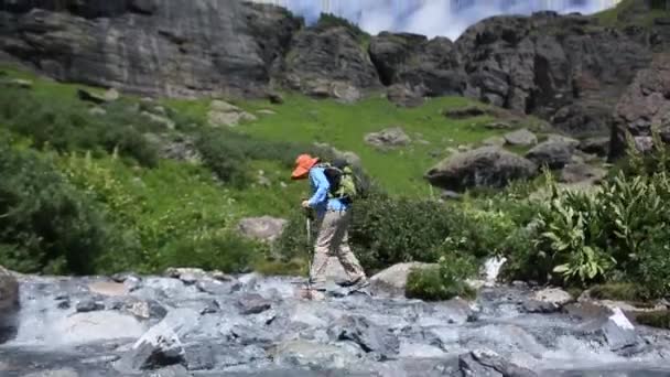 高山草原の小川を渡る女性のハイキング — ストック動画
